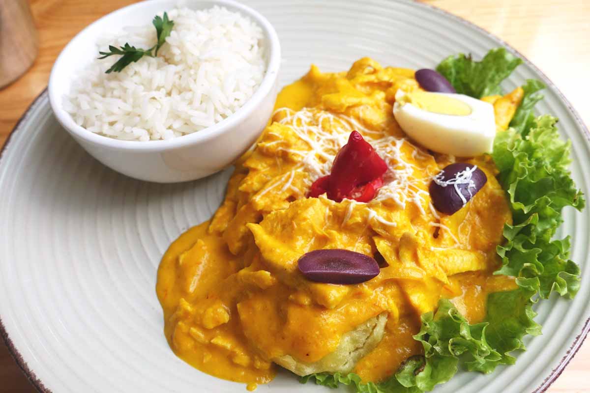 A typical serving of aji de gallina. Orange sauce covering chicken chunks with a white bowl of white rice.