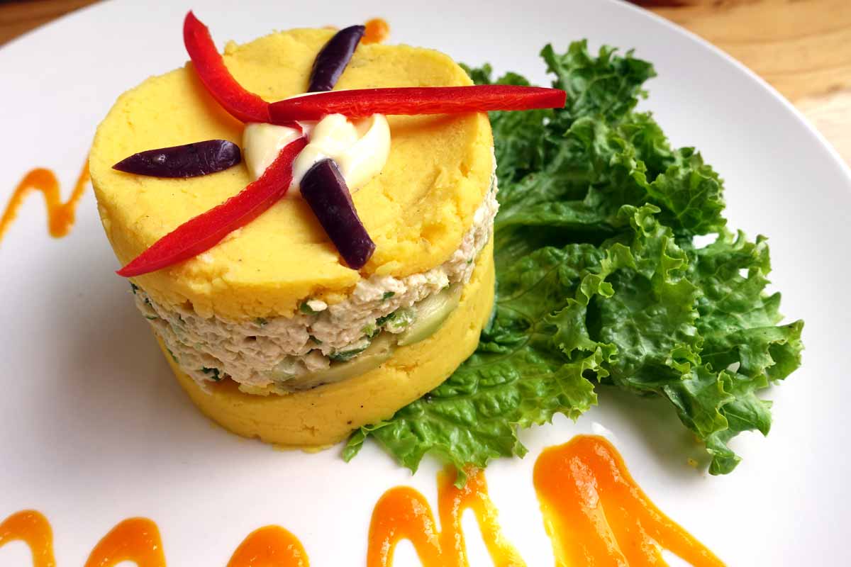 a cylindrical pile of yellow potatoes - made yellow by the addition of turmeric. Layer one is potatoes. Layer two is a sort of chicken salad. Layer three is more yellow potatoes. It's topped with peppers and black olives and served with an orange mango sauce.